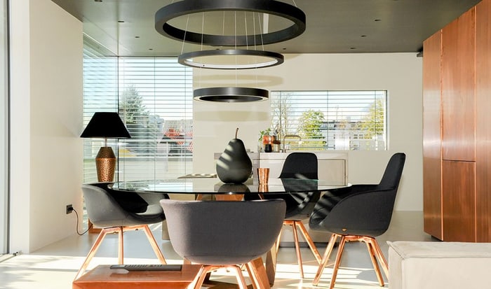 Modernes Esszimmer mit ovalem Glastisch, vier schwarzen Stühlen und zwei runden Pendelleuchten.