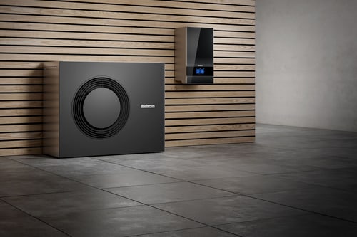Schwarze Buderus Wärmepumpe und Wandthermostat vor einer Holzwand mit Betonboden.